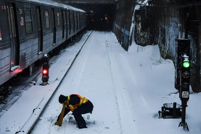 A Q Train Operator clears a snowbound signal stop arm on the above-ground snow-covered subway tracks south of Church Avenue.